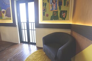 A room with a dark blue armchair, a wooden floor, a yellow rug, and a door with a black gate.