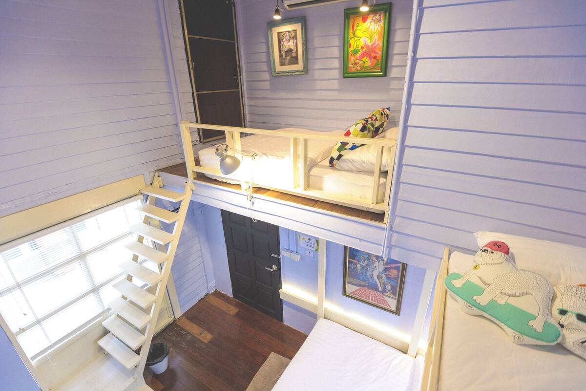 A room with a bunk bed, a window with blinds, a door, and a wall with two framed pictures.