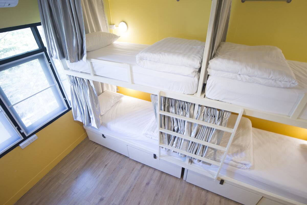 A bunk bed room with a window, curtains, and a wall-mounted light.