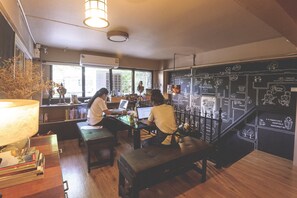 A cozy workspace with two individuals at desks, a large window, and a wall with a chalkboard design. - Bharani Hostel (Bangkok)
