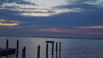 Un tramonto su una superficie d'acqua calma, con un molo e diverse paline in primo piano.