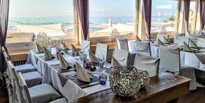 A dining area with tables set for a meal, overlooking a beach with boats and umbrellas. - Bodenseehotel Weisses Rössli (Thal)