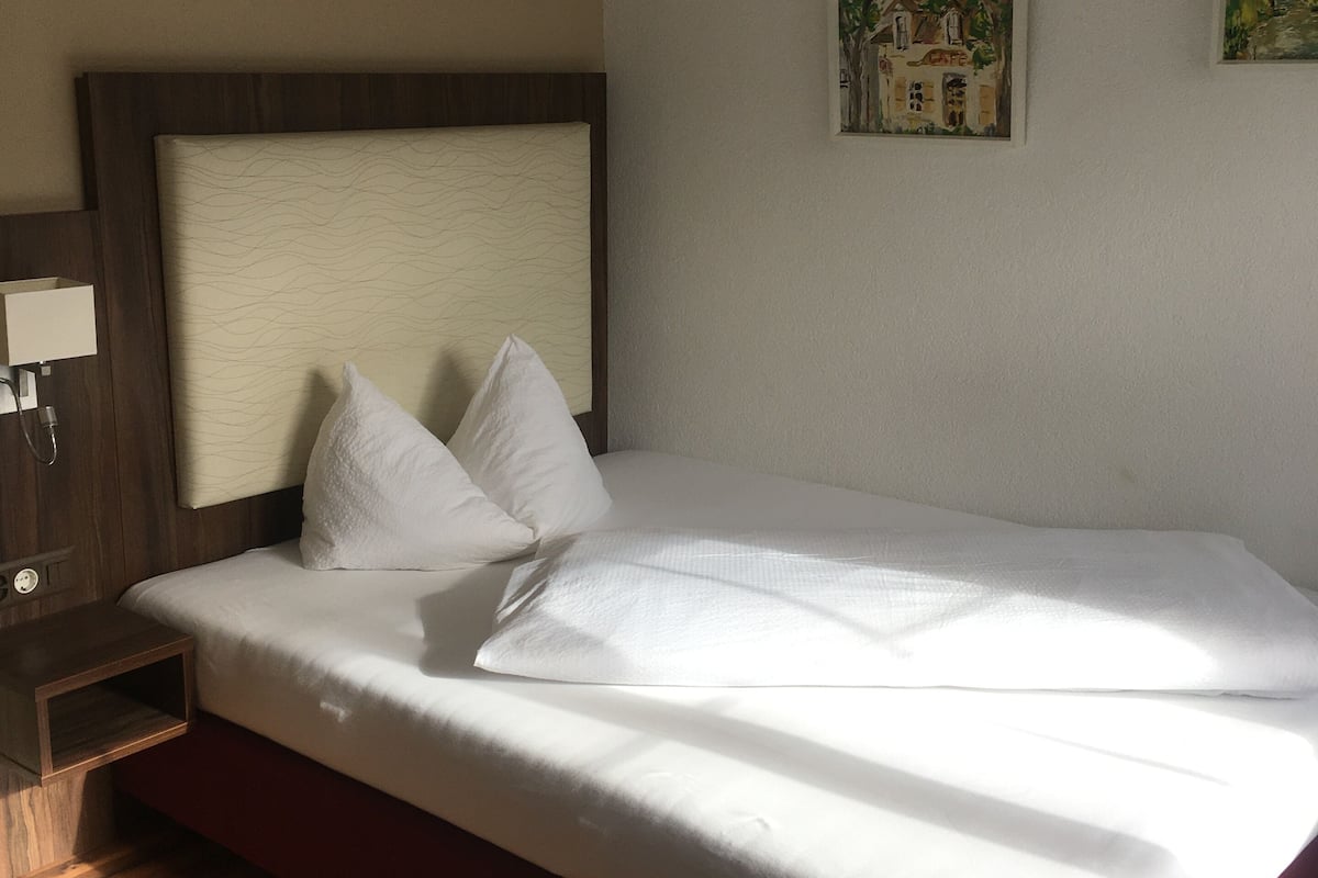 Et hotelv ærelse med en stor seng, trægulv, et natbord, en lampe og to billeder hængt på væggen.