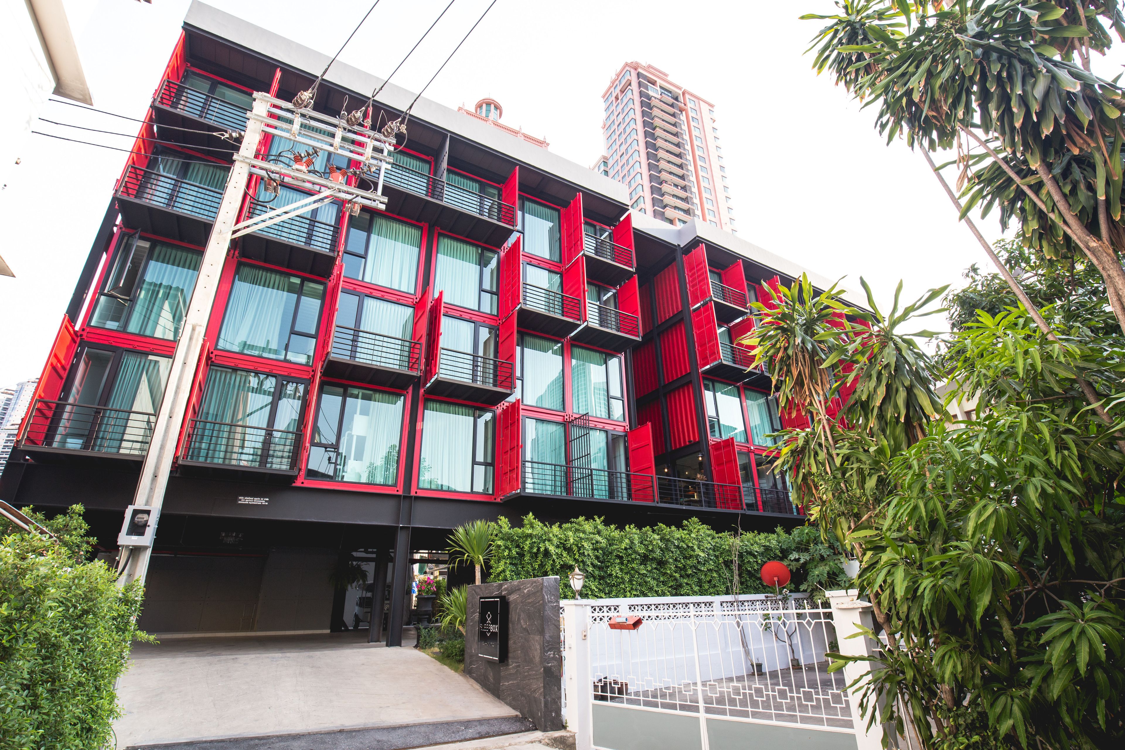 A modern building with multiple balconies, a gated entrance, and surrounding greenery.