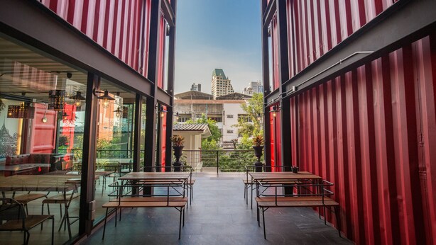 A modern cafe with red-striped walls, outdoor seating, and a view of buildings in the background. - Sleep Box Sukhumvit 22 (Bangkok)