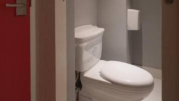 A modern bathroom with a toilet, a hand dryer, and a framed picture on the wall.