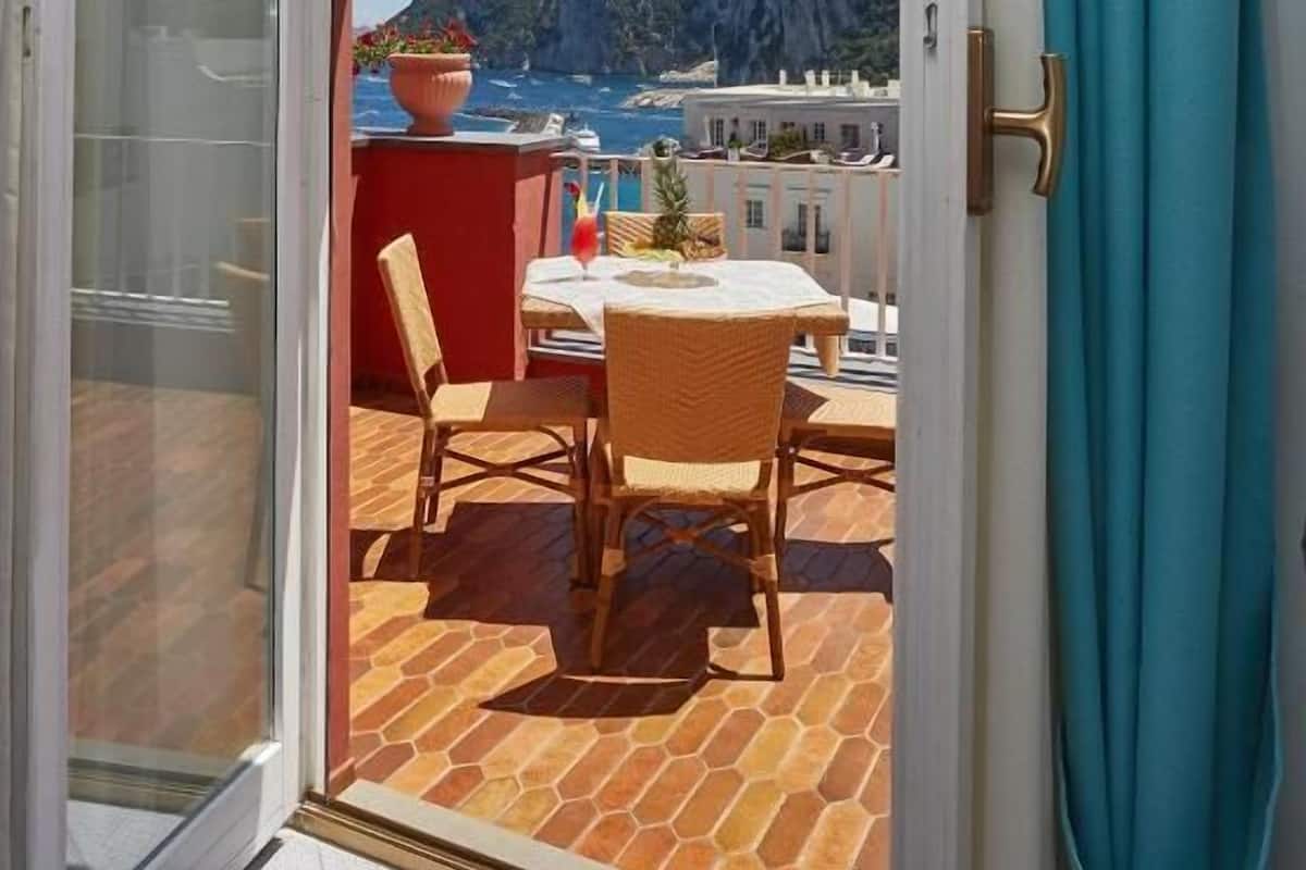 Un balcón abierto con una mesa y sillas, una planta en maceta y vistas al mar y los acantilados.