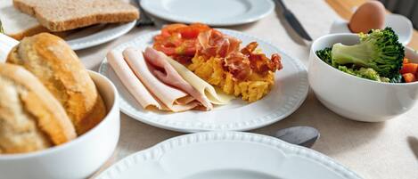 A breakfast setting with plates of toast, ham, eggs, and vegetables.