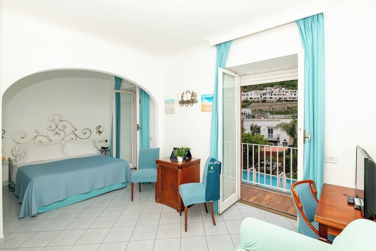Un dormitorio con cama, escritorio, silla y balcón con vistas.