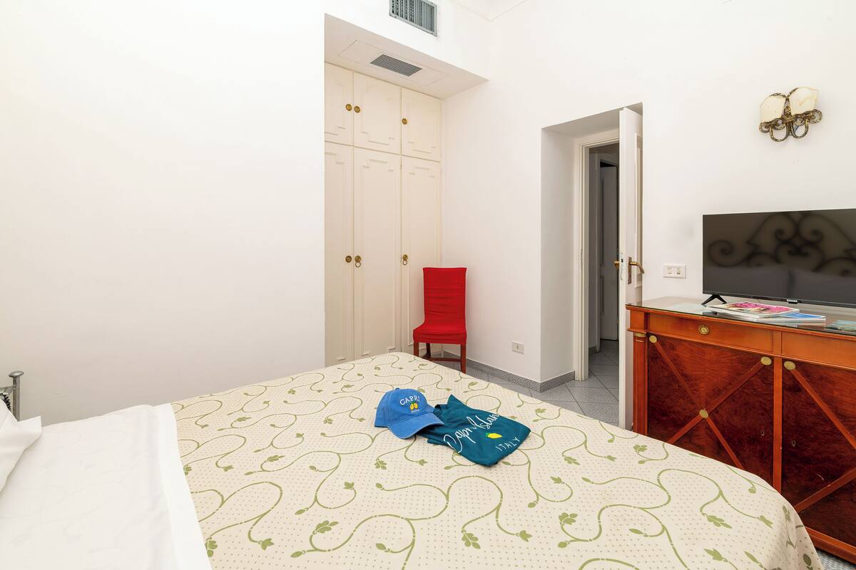 Un dormitorio con una cama, una silla roja, un aparador de madera y un televisor.