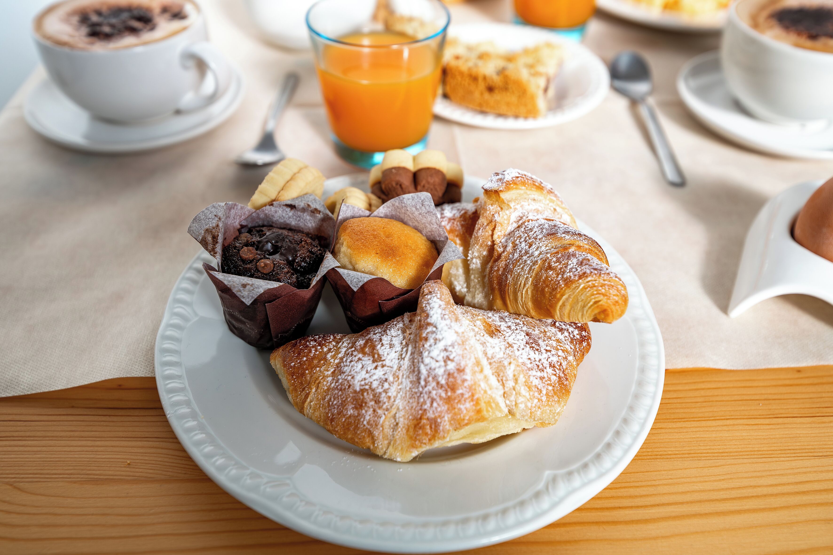 Ein Frühstückstisch mit Gebäck, einer Kaffeetasse und einem Glas Orangensaft.