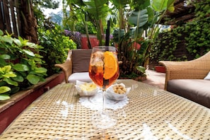 A wicker table with a glass of iced tea and an orange slice, surrounded by greenery and wicker furniture. - Hotel Palatium Mari (Capri)