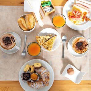 Una mesa con una variedad de alimentos para el desayuno: pan, huevos, tocino y bebidas.