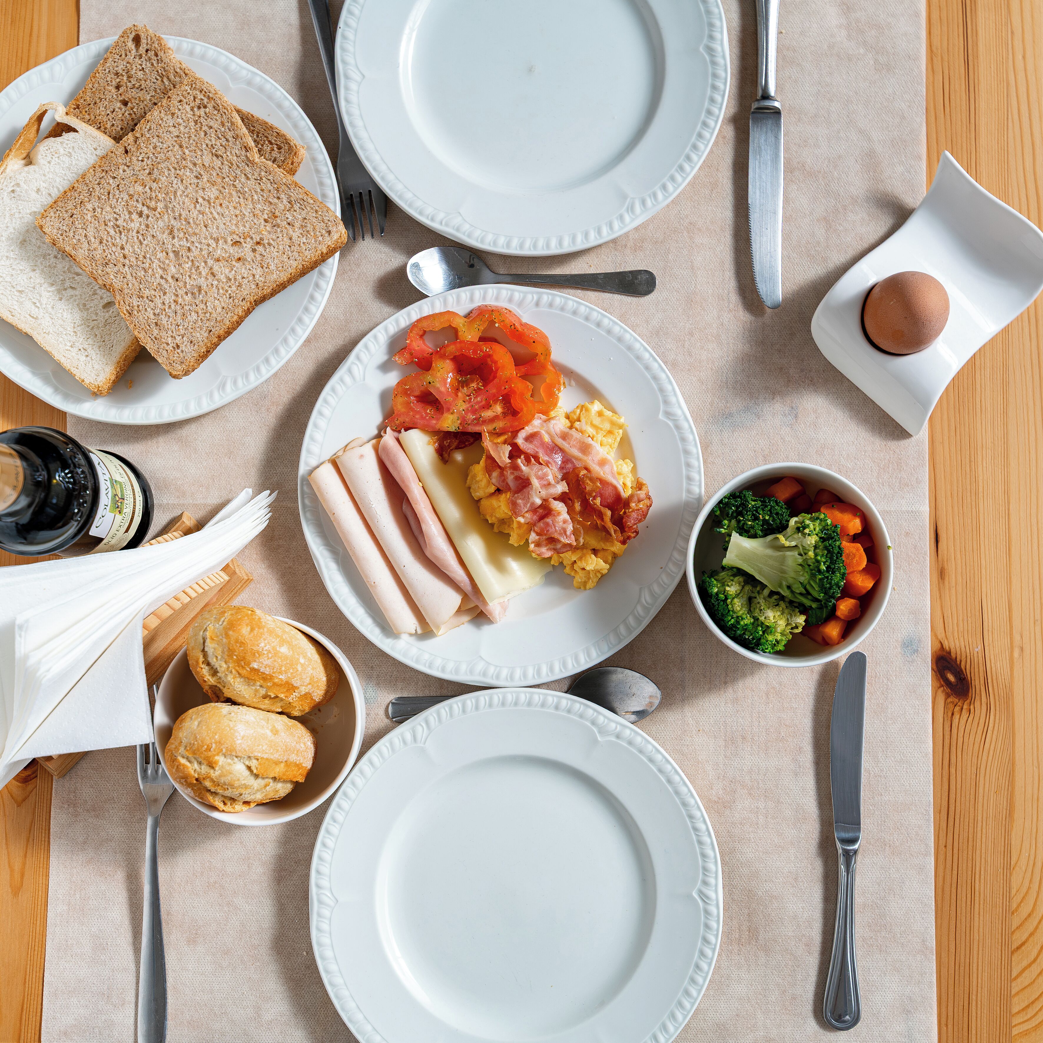 A breakfast setting with plates of toast, eggs, bacon, and vegetables.