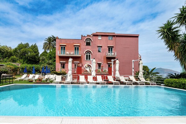 Un hotel con piscina, sillas de descanso y sombrillas.