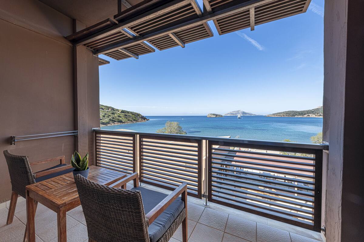 A balcony with a view of the sea, a wooden table, and wicker chairs.