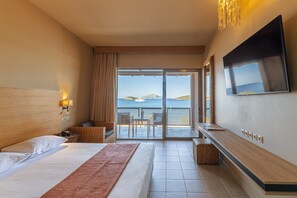 A hotel room with a bed, a TV, a balcony with a view of the sea, and a table with chairs. - Aegeon Beach Hotel (Lavreotiki)