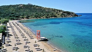 A beach with rows of sunbeds and umbrellas, a lifeguard tower, and clear blue water. - Aegeon Beach Hotel (Lavreotiki)
