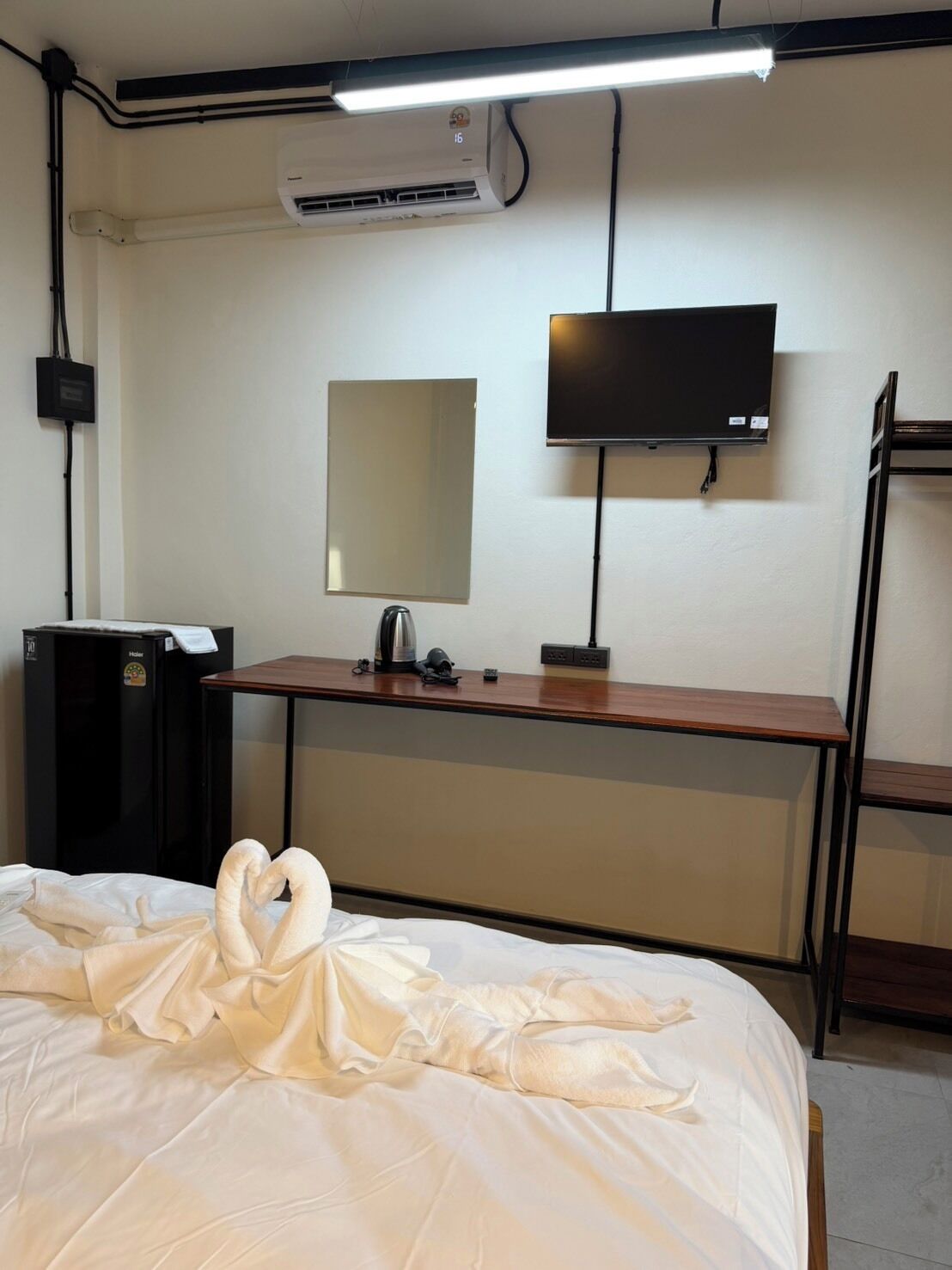 A hotel room with a bed, a desk, a flat-screen TV, a mirror, an air conditioner, and a heater.