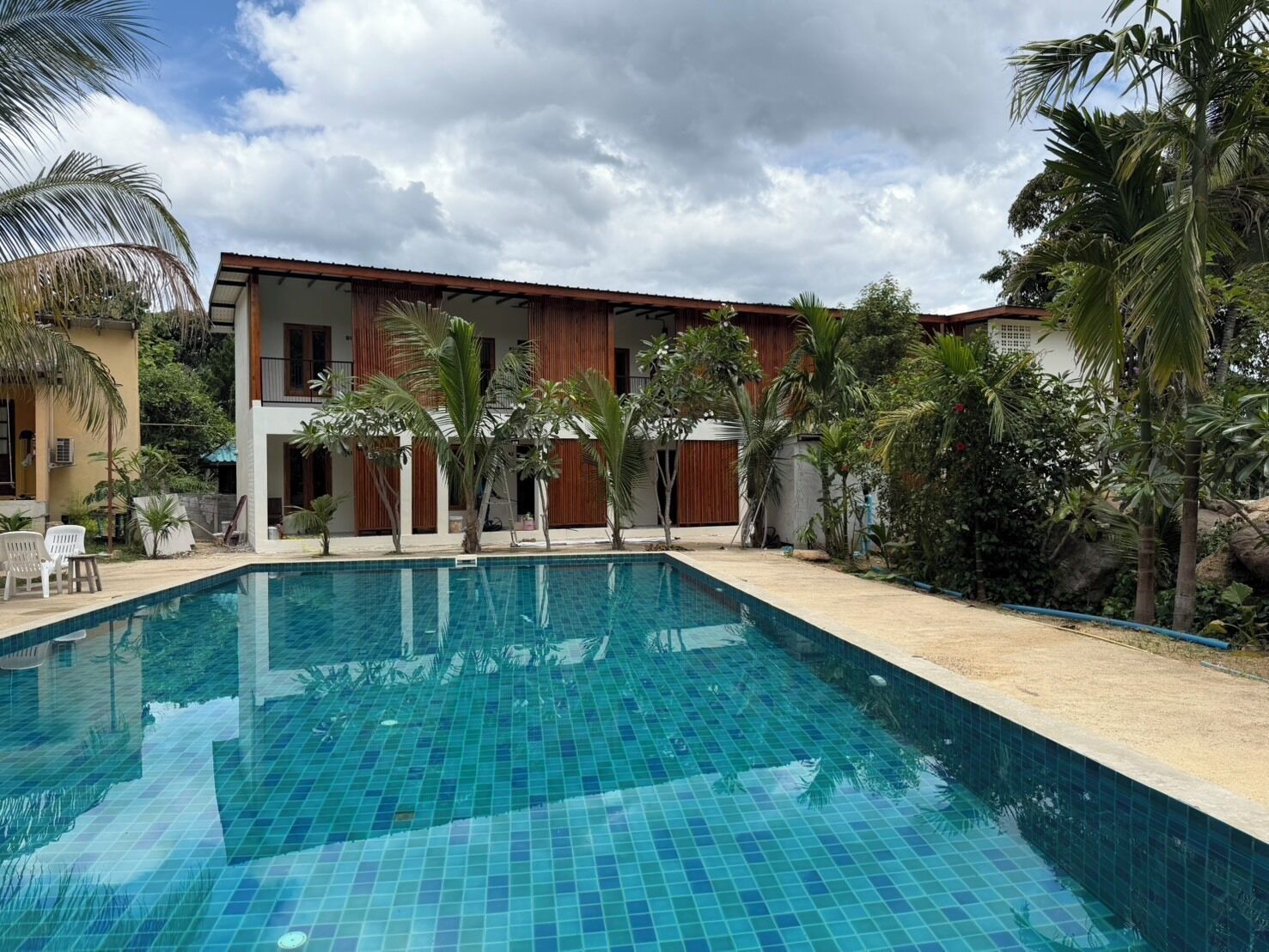 Una piscina con superficie azulejada, rodeada de palmeras y un edificio de techo rojo.