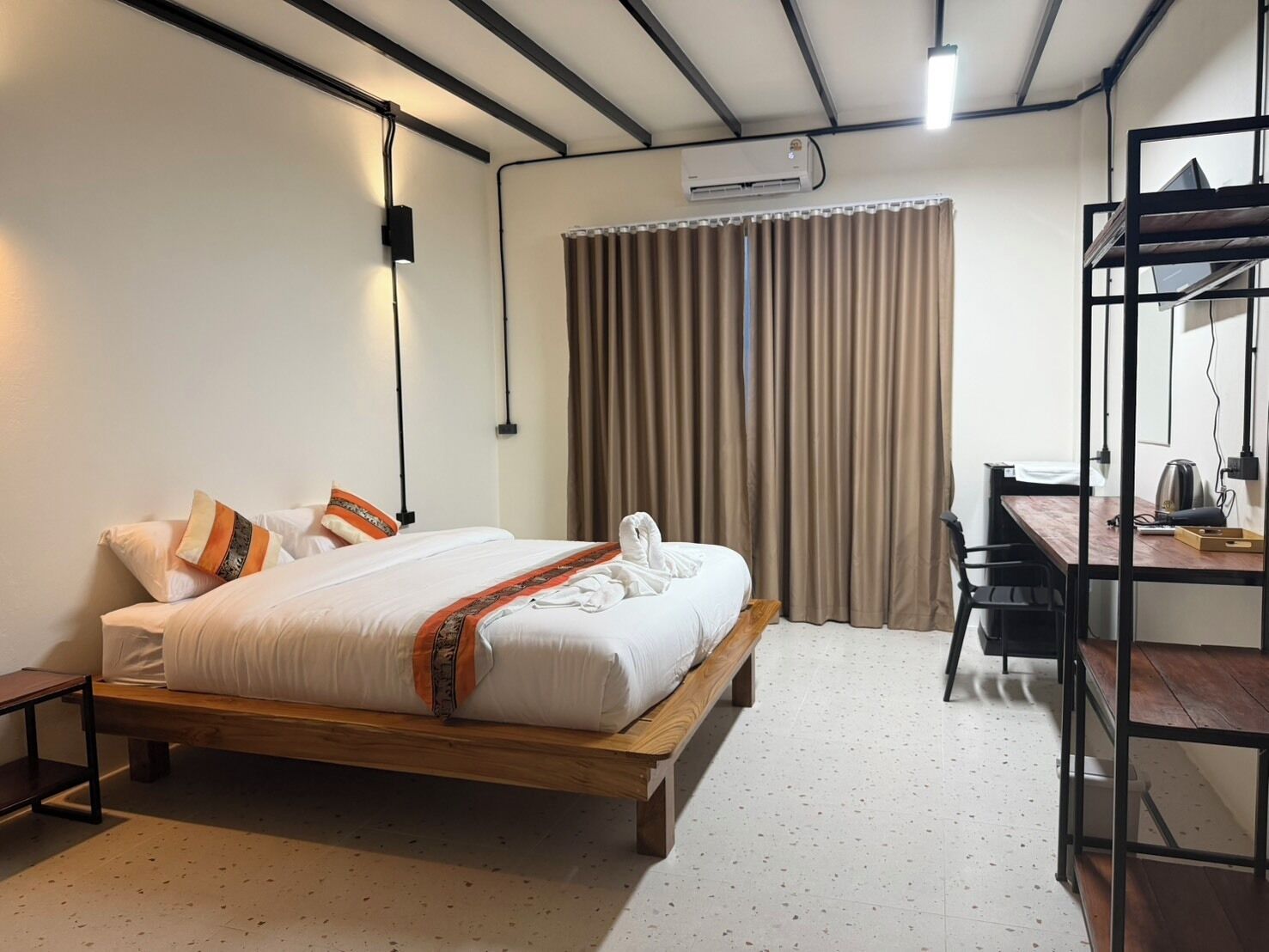 A hotel room with a bed, a desk, a chair, an air conditioning unit, and a curtain.