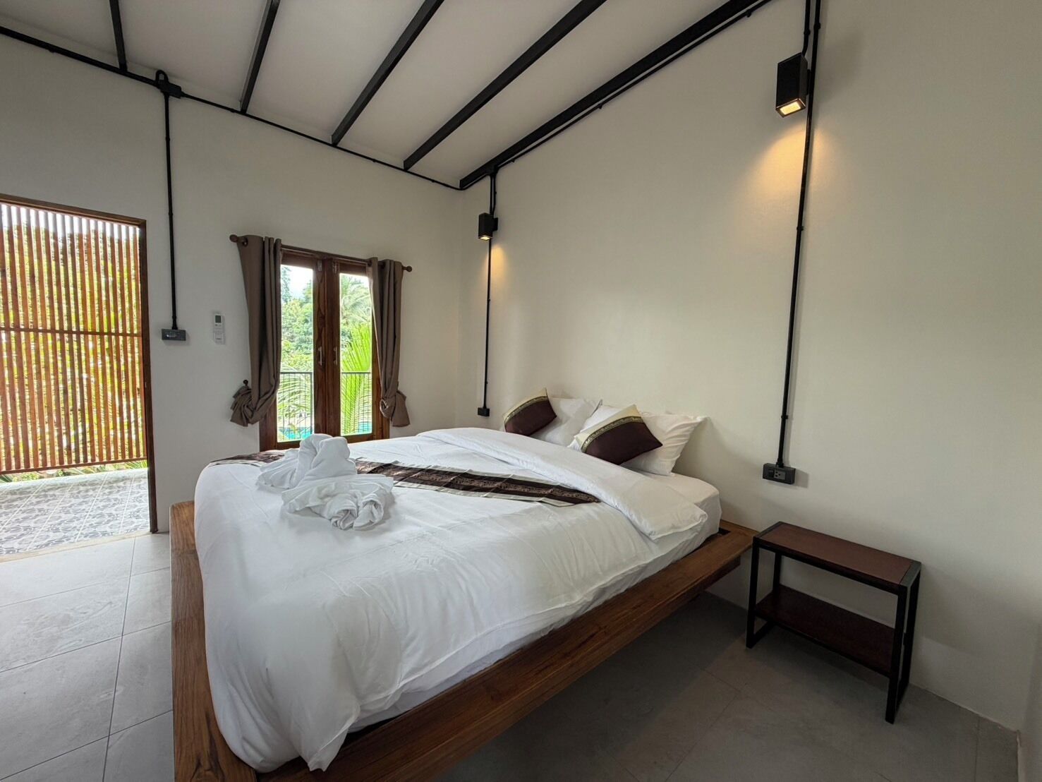 A modern bedroom with a bed, bedside table, and a view through a window.