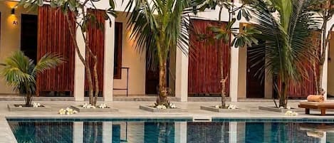 Piscina con el reflejo de palmeras y un edificio de revestimiento vertical rojo y balcones.
