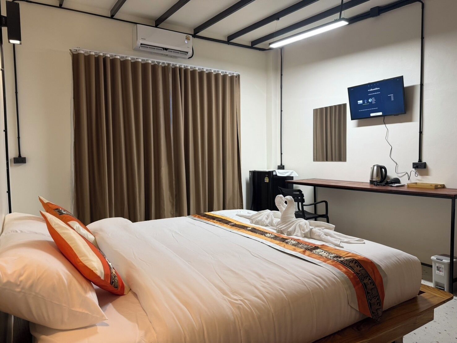 A hotel room with a bed, a desk with a computer, an air conditioner, and a television.