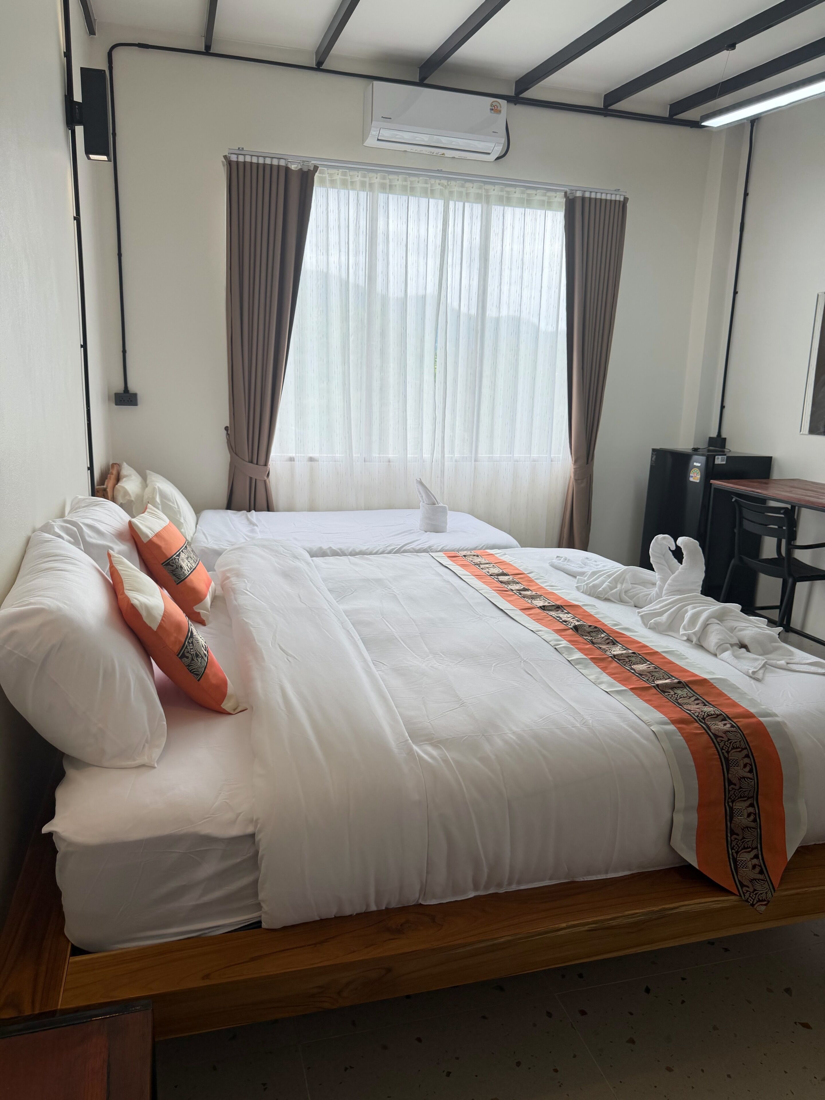 A hotel room with two beds, a desk, and an air conditioning unit.