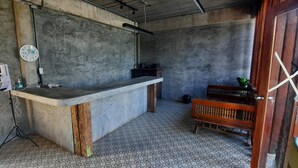 Una habitación pequeña y rústica con un mostrador de hormigón, un banco de madera y suelo de baldosas.