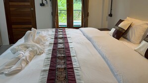 A hotel room with a bed, a window with curtains, and a view of greenery outside.