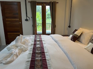 A hotel room with a bed, a window with curtains, and a view of greenery outside. - Mountain Blues Hotel (Pai)