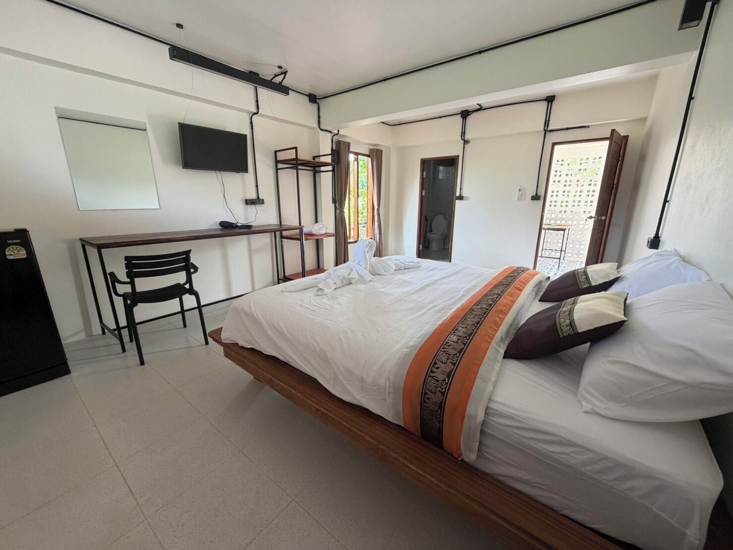 Un dormitorio con cama, escritorio, silla y televisor en la pared.
