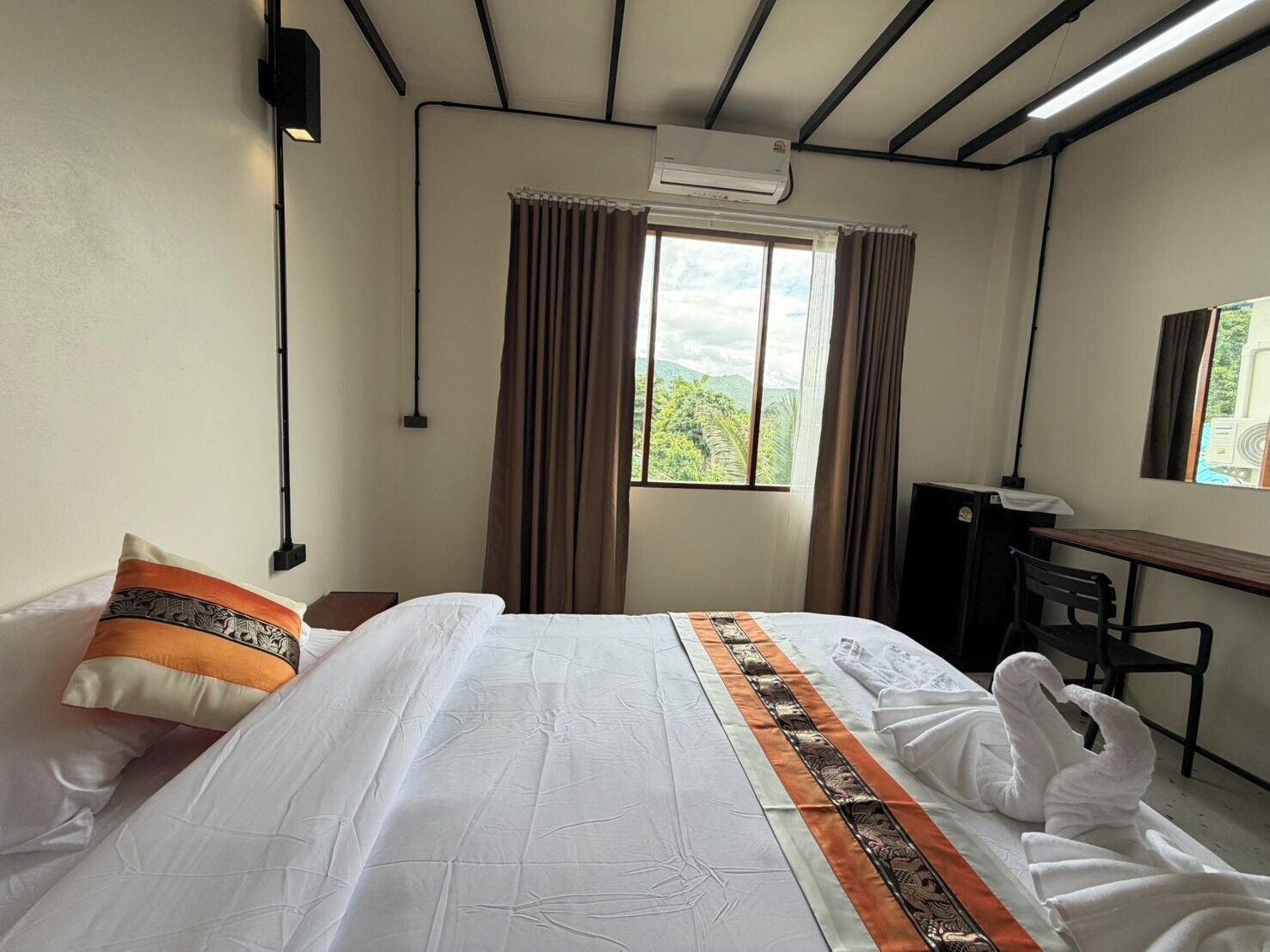 Quarto de hotel com cama, escrivaninha, ar condicionado e janela com cortinas.