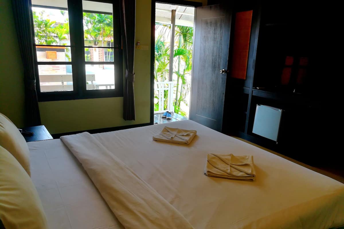 A hotel room with a bed, a window with curtains, a door, and a view of greenery outside.