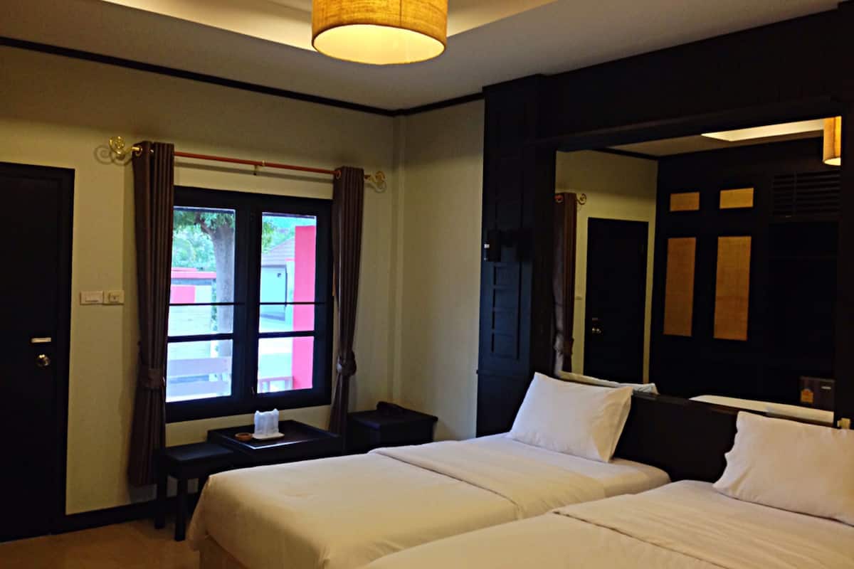 A hotel room with two beds, a window with curtains, a bedside table, and a hanging lamp.