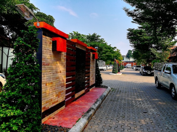 A street with a red and brown building, parked cars, and greenery.