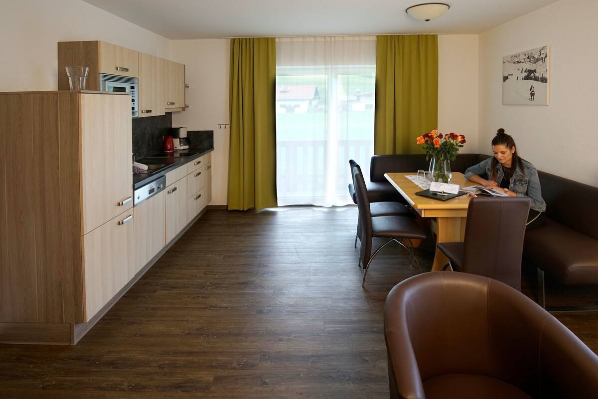 A modern kitchen with wooden cabinets, a dining area with a table and chairs, and a sofa.