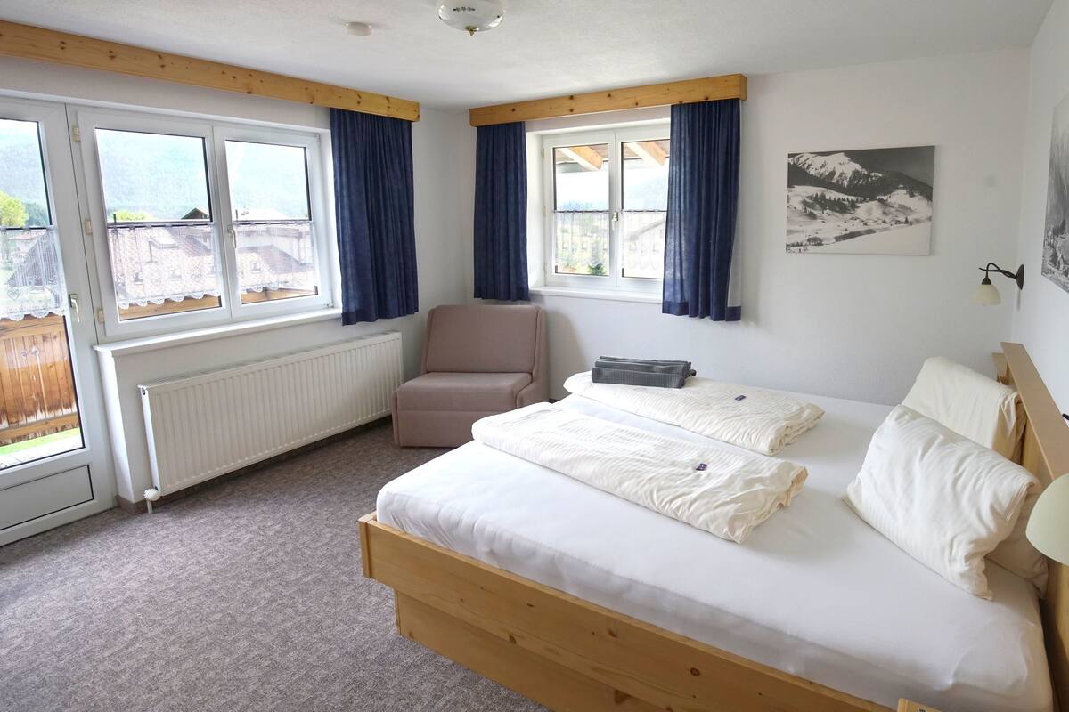 A bedroom with a wooden bed, a chair, a radiator, and a window with curtains.