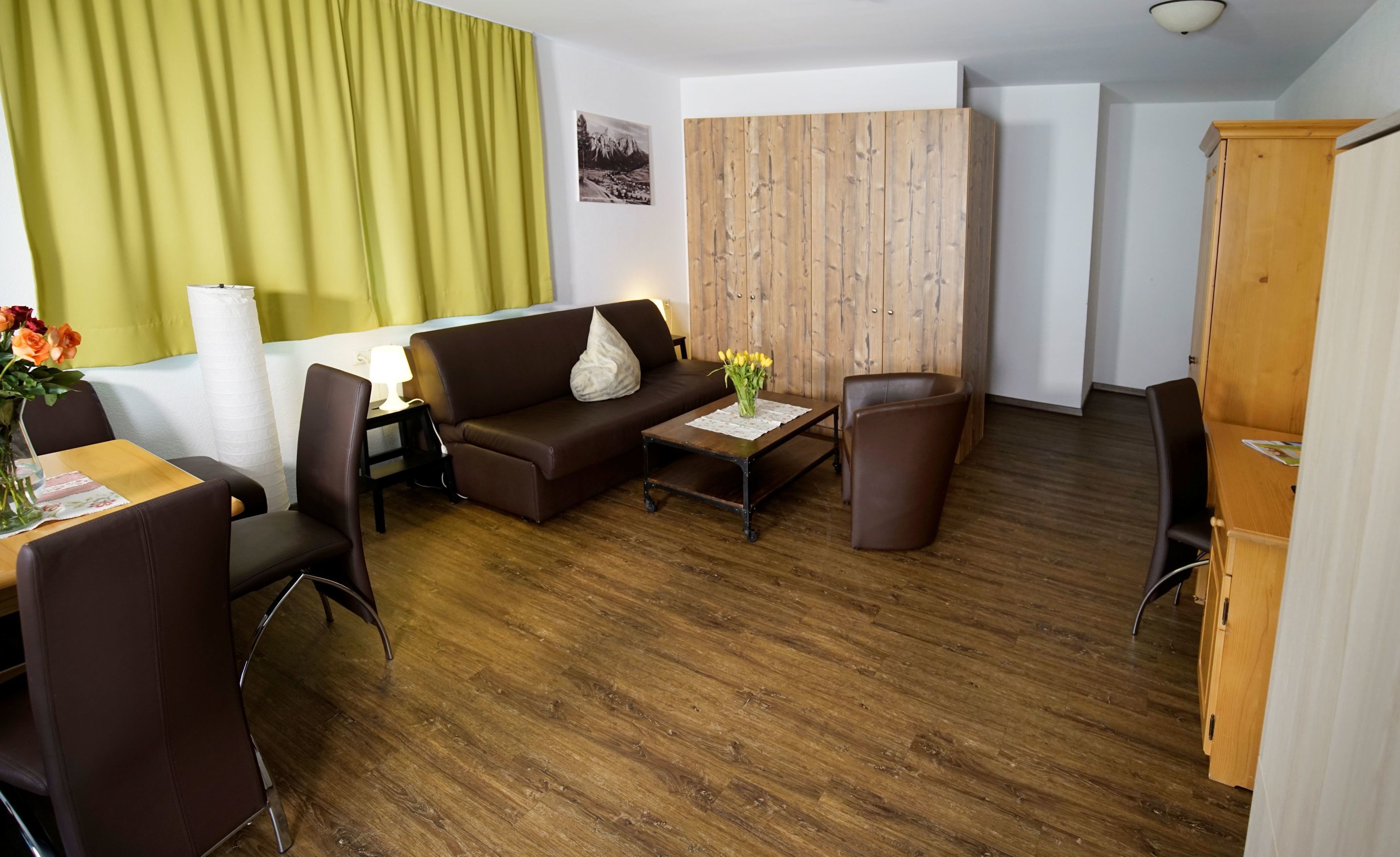 A modern living room with a brown sofa, a wooden coffee table, and a dining area with a table and chairs.