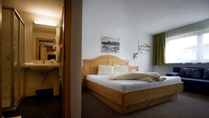 Habitación de hotel con cama de madera, baño con ducha de vidrio y vistas al exterior a través de una ventana.