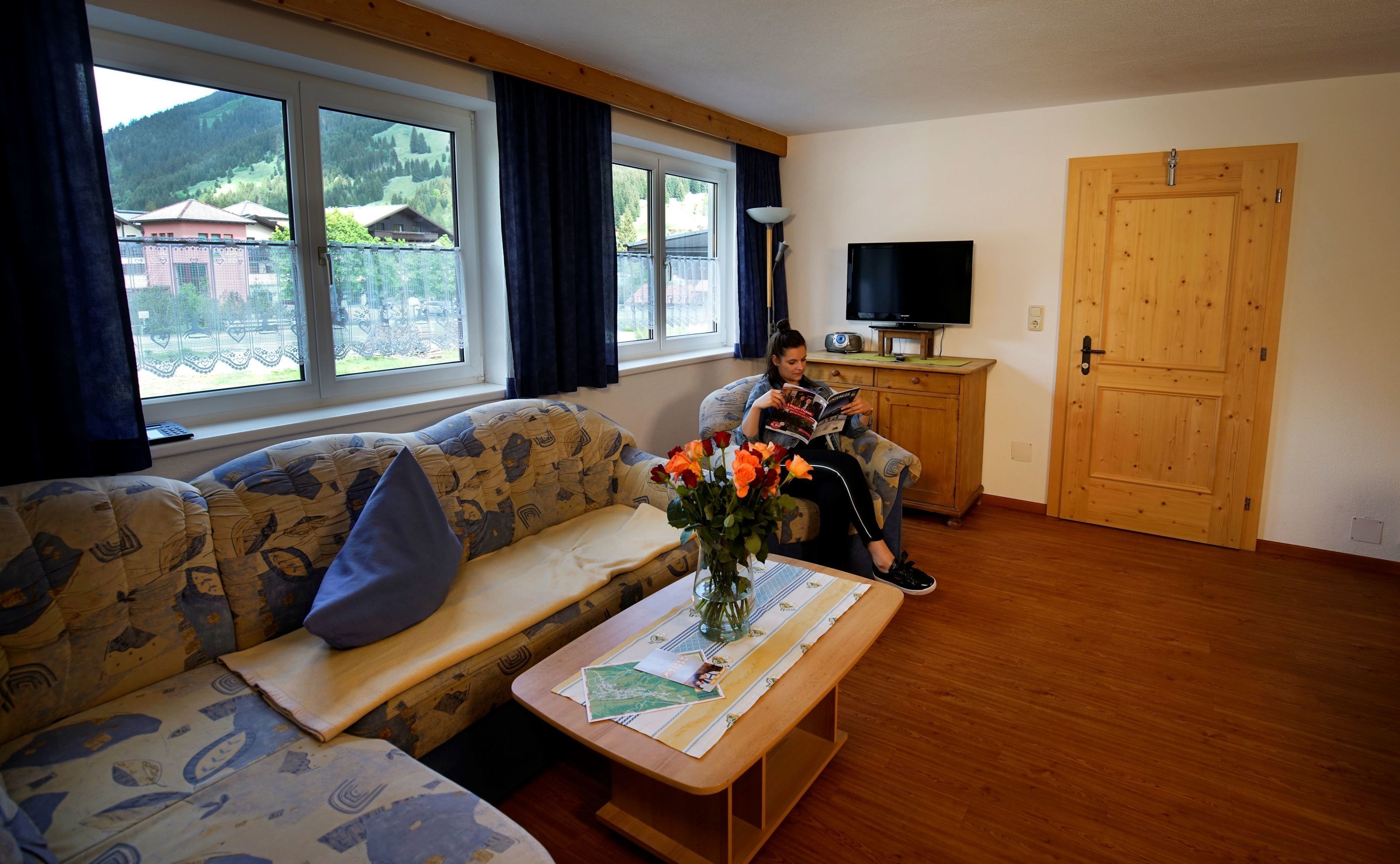 A cozy living room with a sofa, a coffee table with a vase of flowers, a television, and a wooden door.