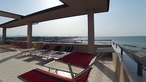 Terraza en la azotea con tumbonas y vista al mar.