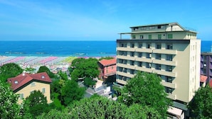 Un hotel de varios pisos con balcones que dan a una playa con sombrillas y gente.