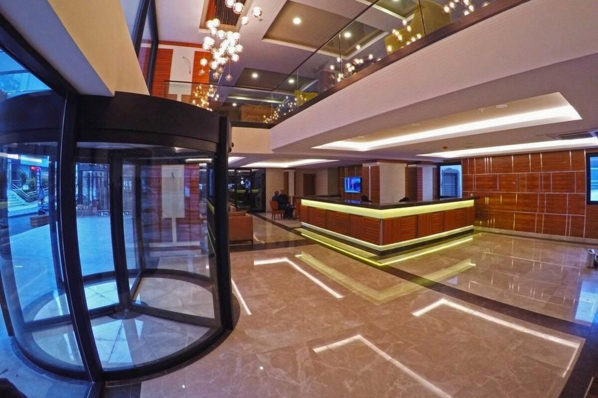 A modern hotel lobby with a revolving door, a reception desk, and a glass elevator.