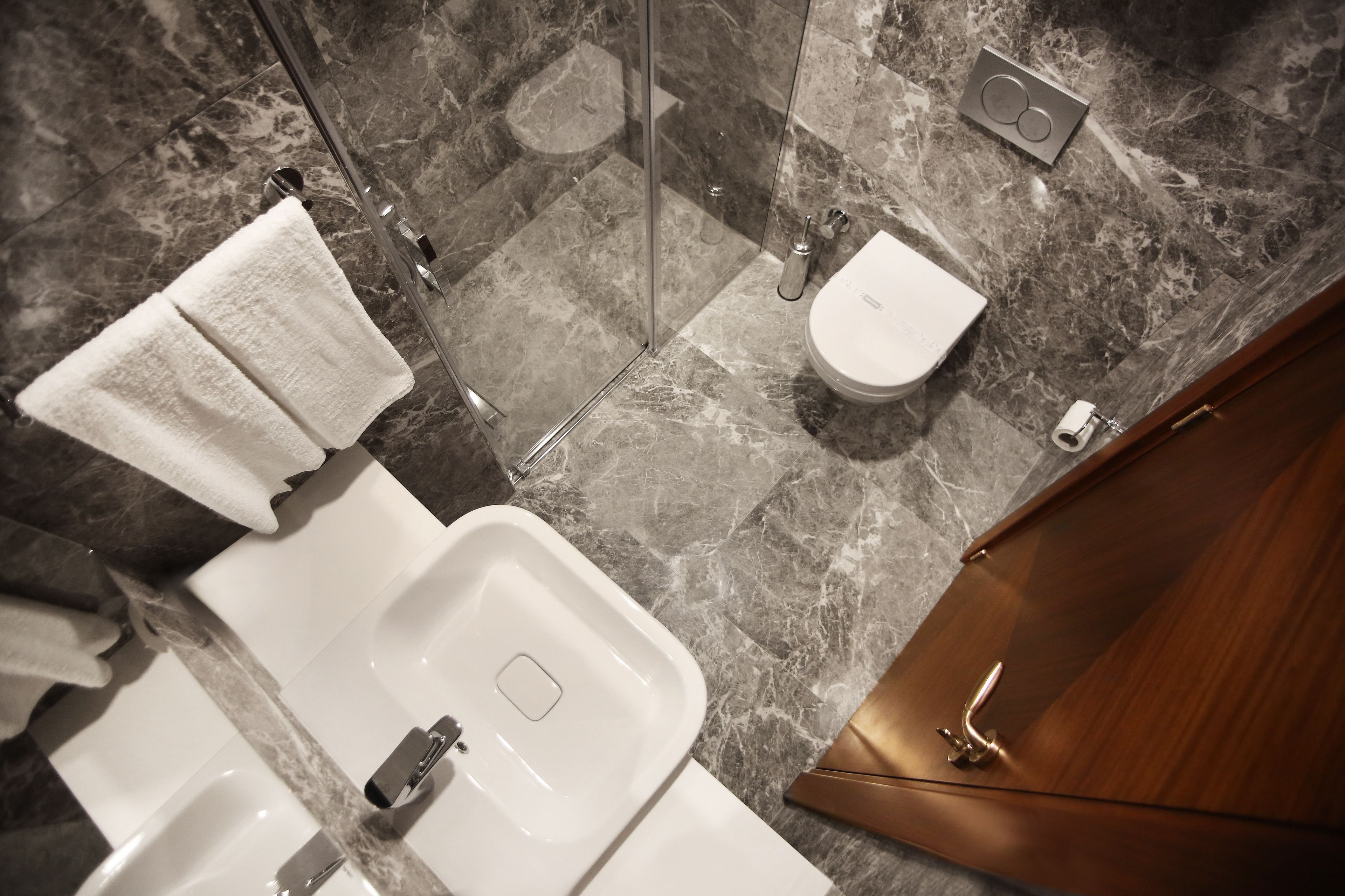 Une salle de bain moderne avec un sol en marbre, un lavabo blanc, des toilettes et un espace douche.