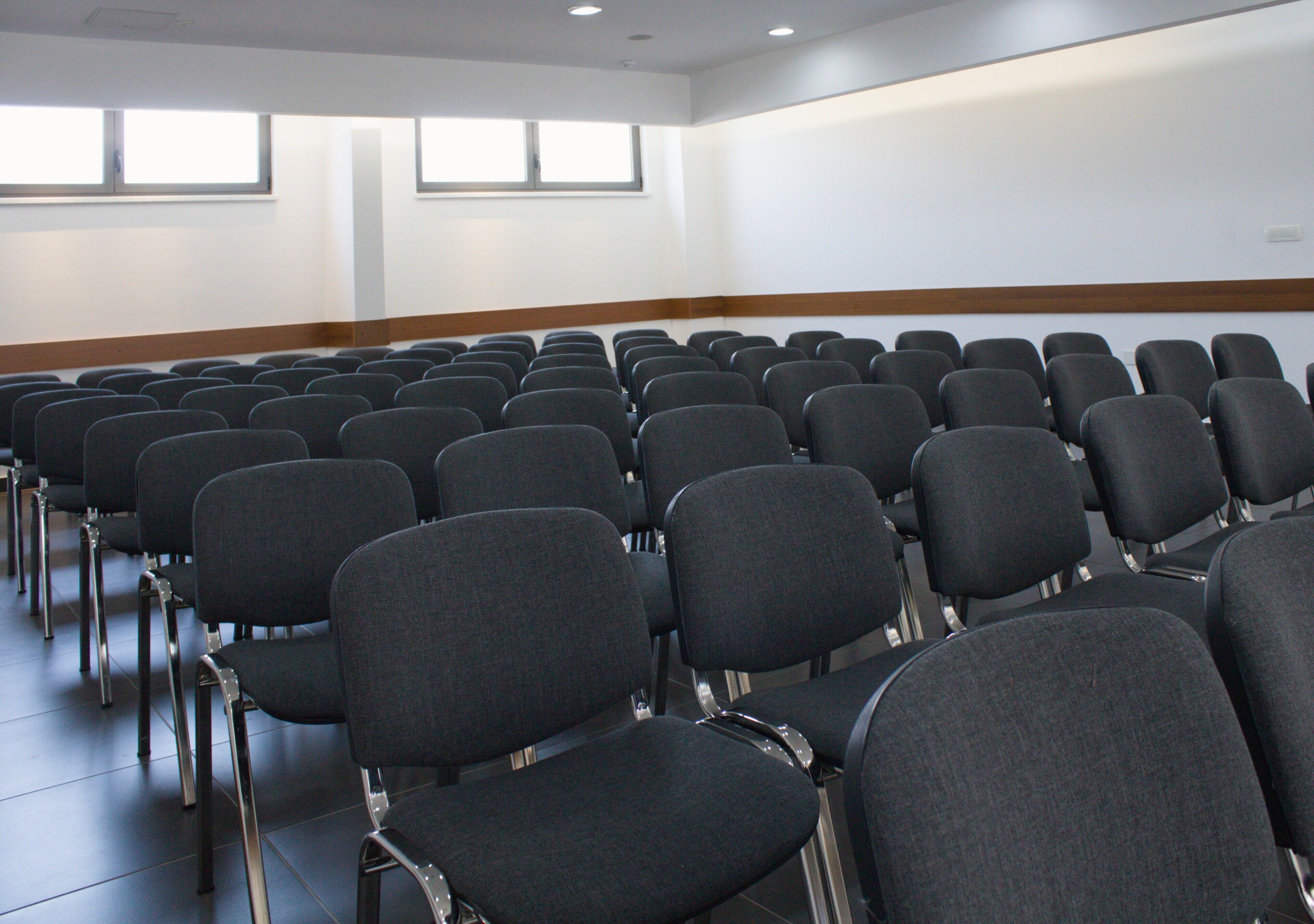 A conference room with rows of black chairs and a wooden panel along the wall.