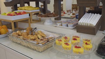 Un bufé con diversas opciones de comida, entre ellas frutas, pasteles y postres.