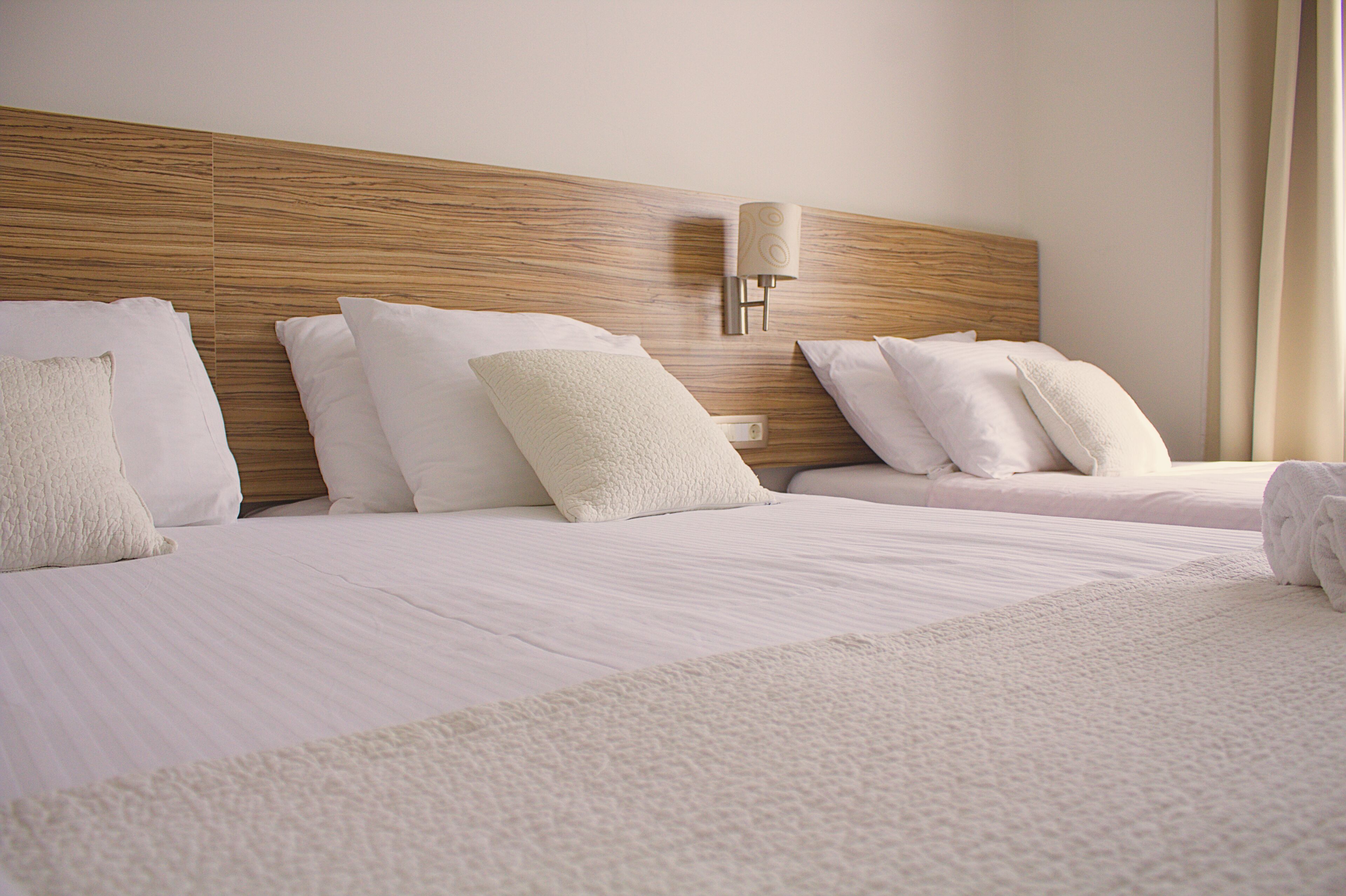 Een hotelkamer met twee bedden, elk voorzien van witte lakens en kussens, een houten hoofdbord en een wandlamp.