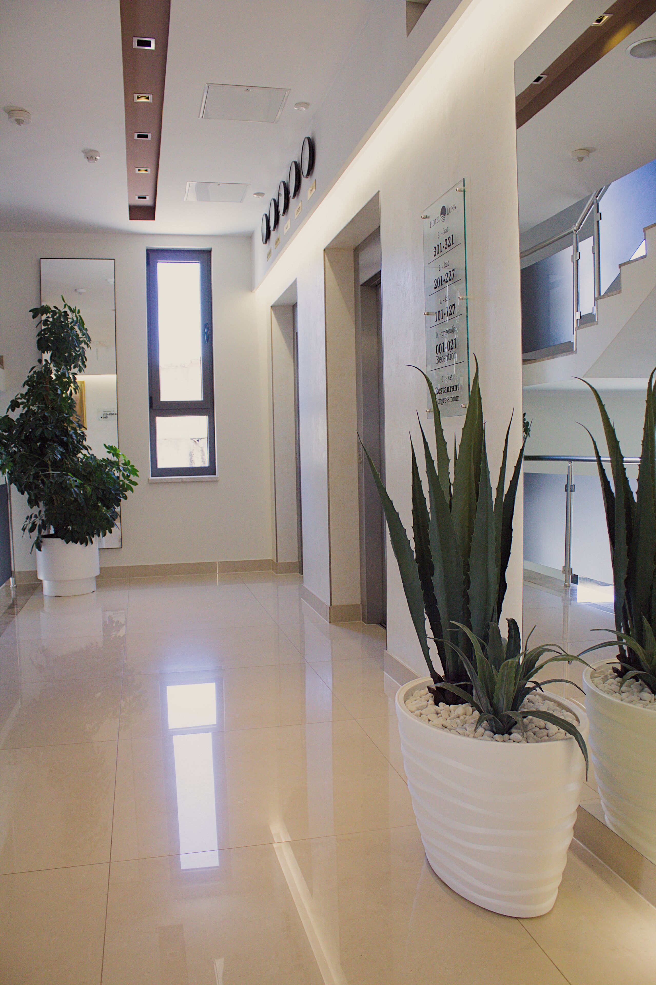 Un pasillo de hotel con una recepción, una planta grande en maceta y una escalera.